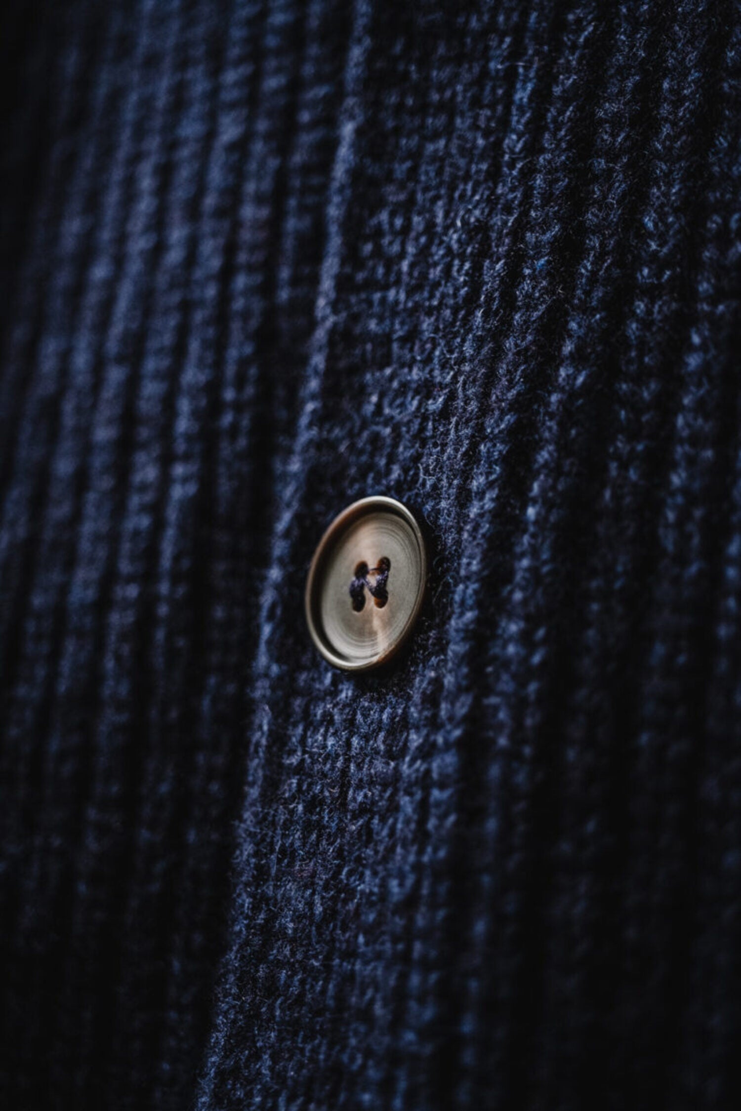 Macro shot of the denim blue wool texture and classic button detail of the Lobo Apparel cardigan.