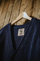 Top detail of the denim blue cardigan on a wooden hanger, showing the Lobo Apparel label and V-neckline.