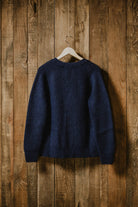 Back view of the Lobo Apparel denim blue wool cardigan hanging against a rustic wooden wall.