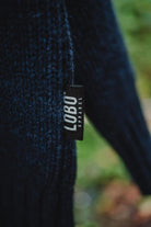 Detail of the black LOBO Apparel logo label sewn onto the side of the blue knit sweater.