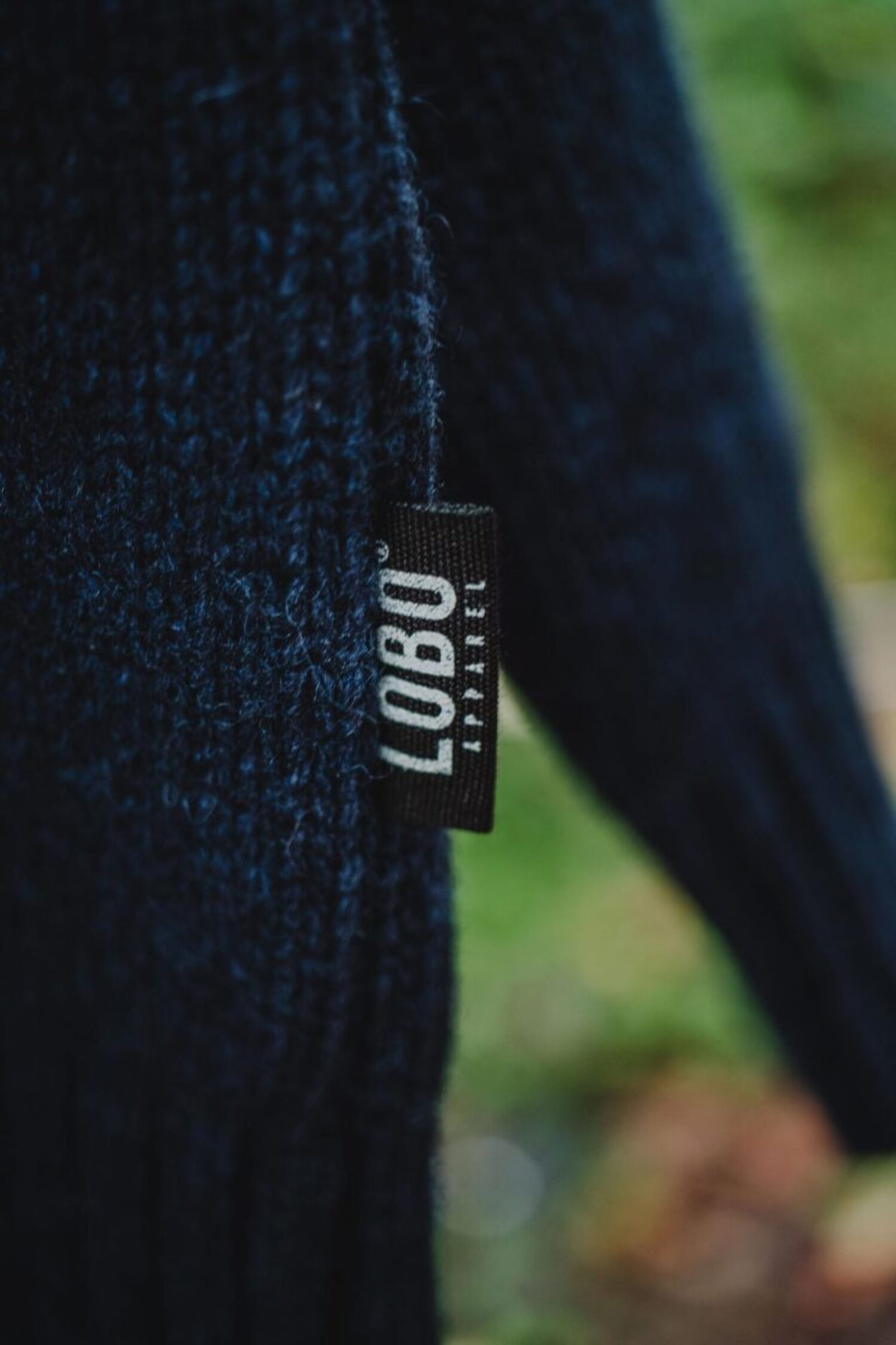 Detail of the black LOBO Apparel logo label sewn onto the side of the blue knit sweater.