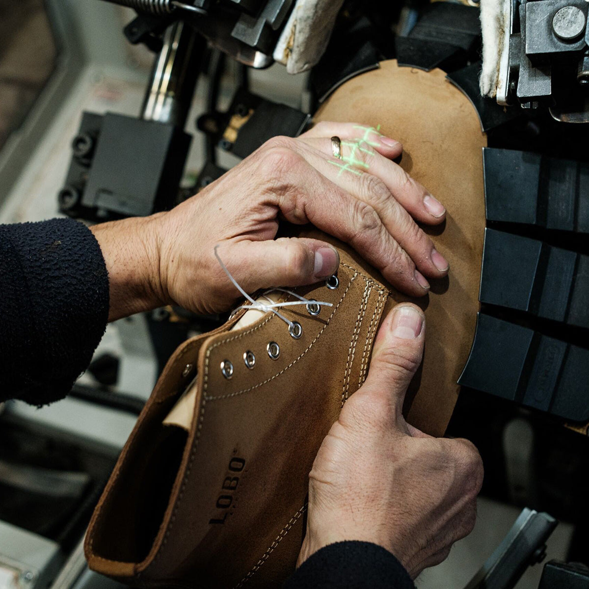 Hands of a craftsman precisely adjusting a LOBO brand brown leather boot on a shoe-lasting machine. Detail of the technical and artisanal high-quality boot manufacturing process.