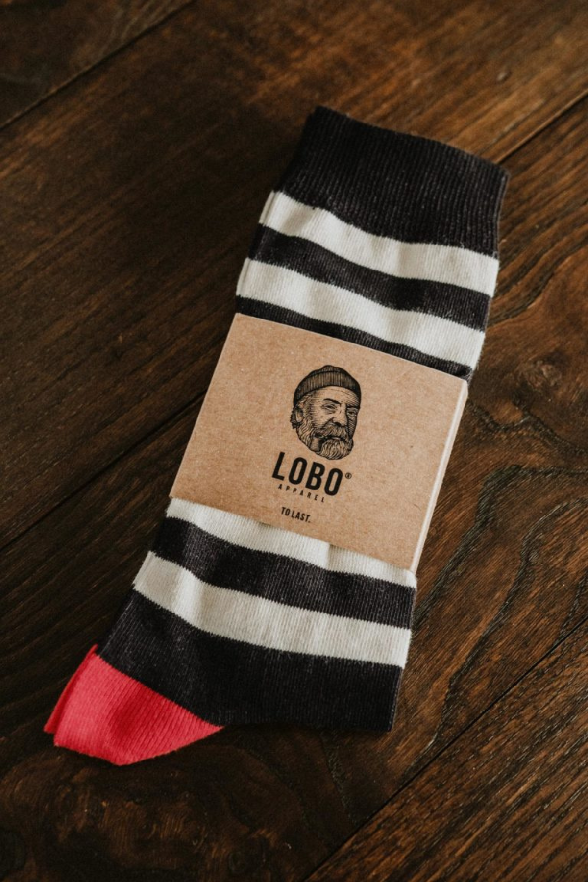 Lobo black and white striped socks with red heel detail and eco-friendly cardboard packaging on a wooden surface.
