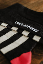 Close-up of the "Lobo Apparel" logo embroidered in white on premium black knit socks.