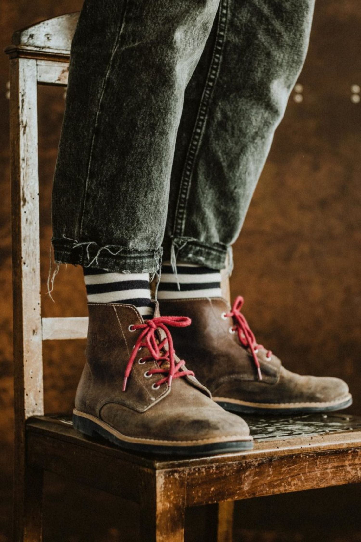 Person standing on a vintage wooden chair wearing Lobo Black Stripes socks and boots with red laces.