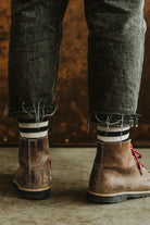 Detail of Lobo striped socks worn with brown leather boots and frayed grey denim jeans, back view.