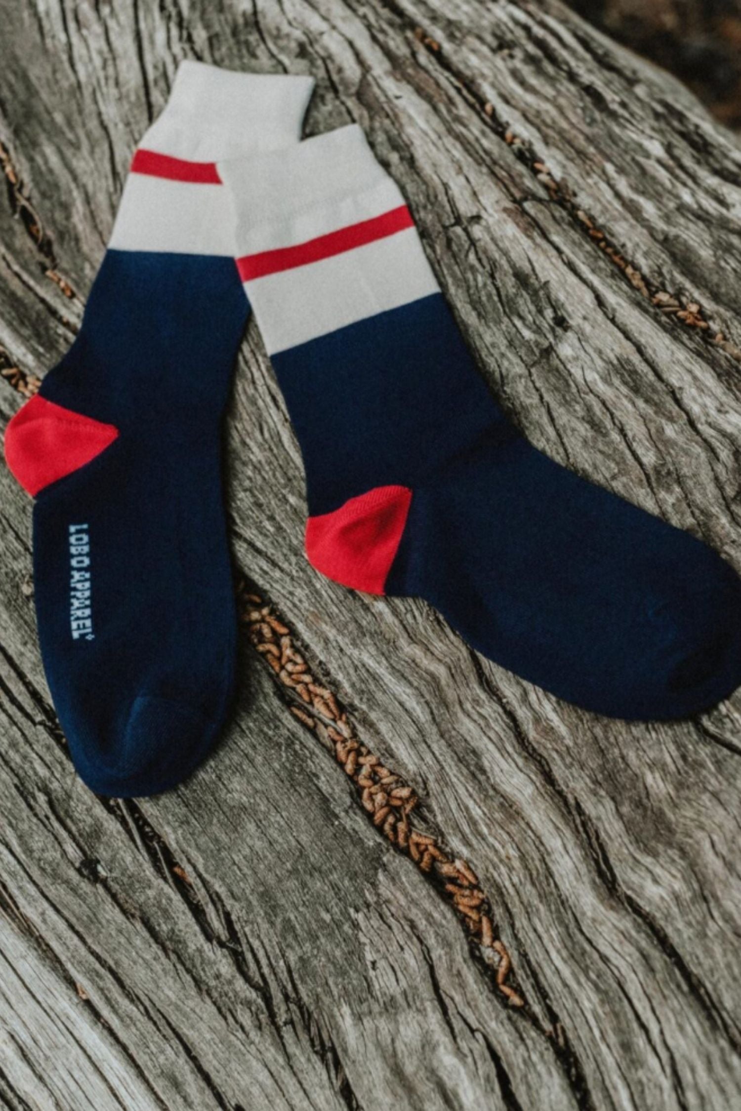 Pair of Lobo Blue Socks in dark blue and white with a red stripe, resting on a rustic wooden log.