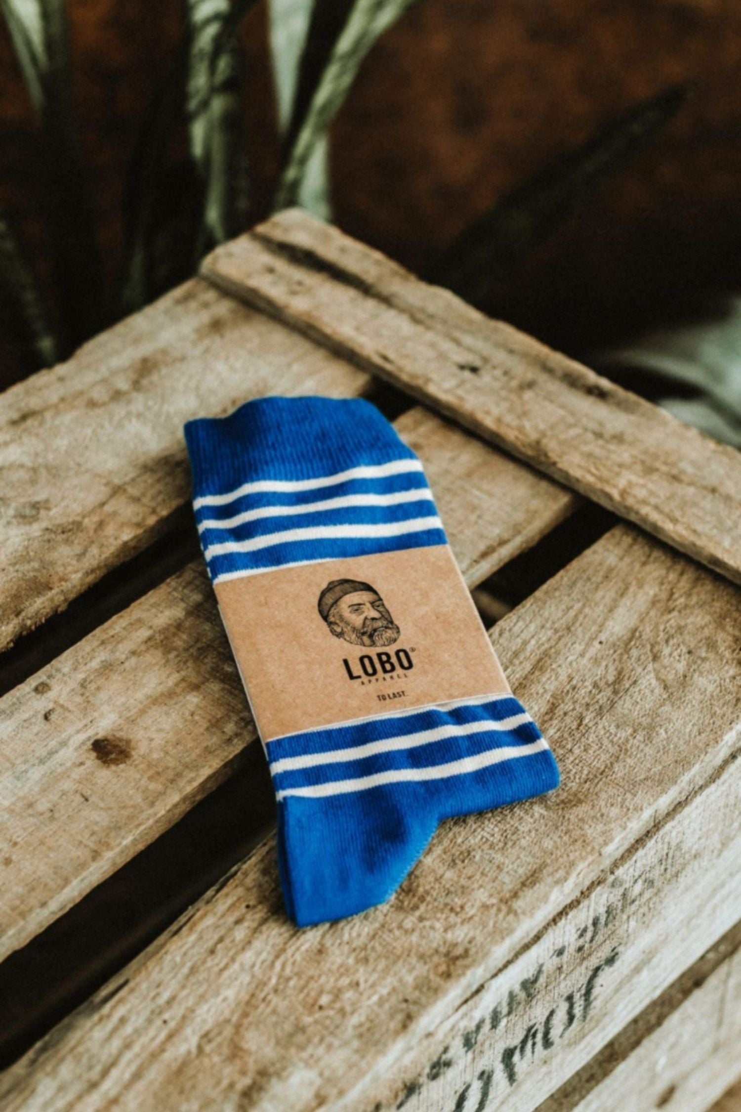 Lobo Blue Stripes Socks made from premium natural fibers in blue with white stripes, featuring kraft paper packaging on a rustic wooden background.