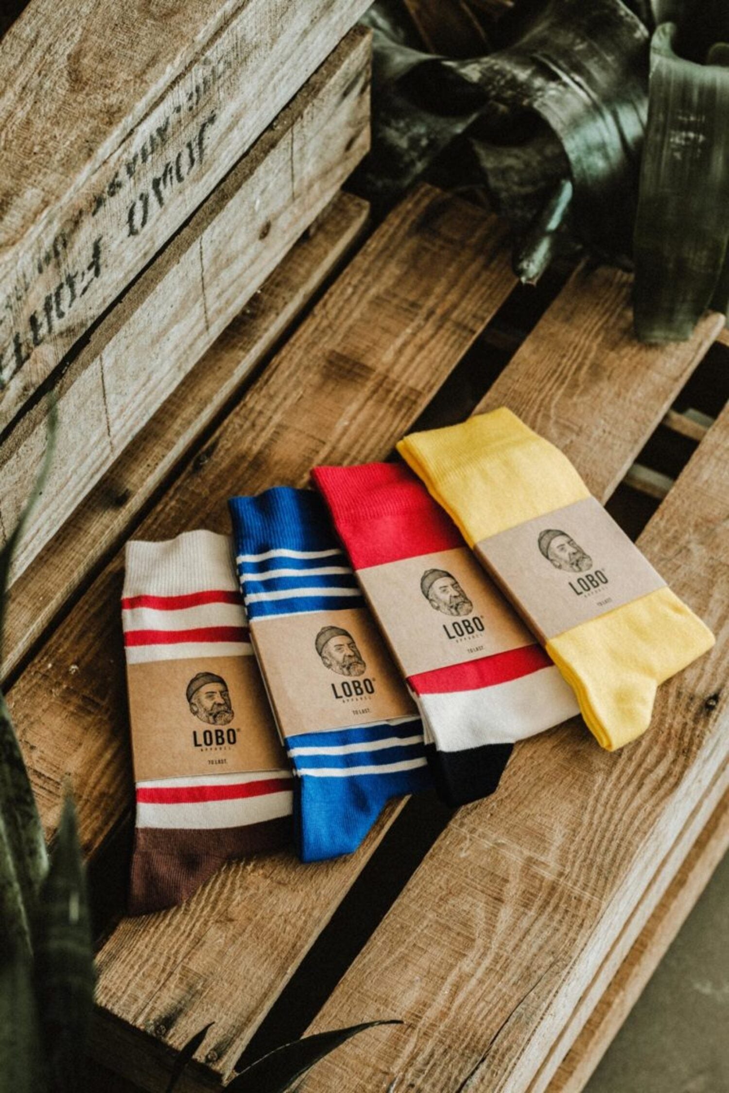 Lobo socks collection made from premium natural fibers, featuring various patterns and colors (blue, red, yellow, and beige) in sustainable packaging on wood.