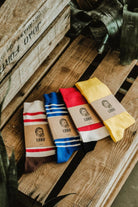 Lobo socks collection made from premium natural fibers, featuring various patterns and colors (blue, red, yellow, and beige) in sustainable packaging on wood.