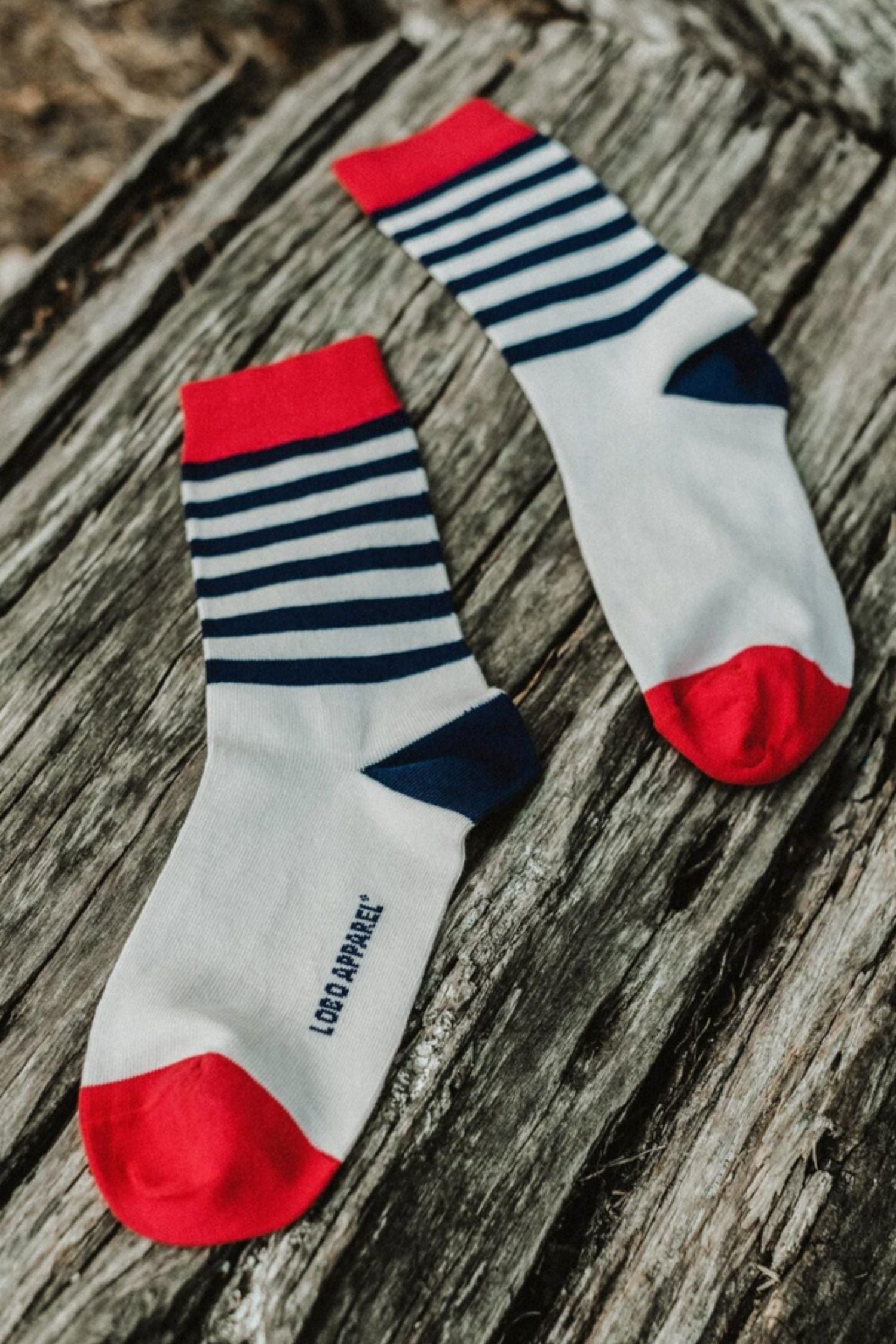 Pair of Lobo blue striped socks with red tops and toes made from premium natural fibers, displayed on rustic wood.
