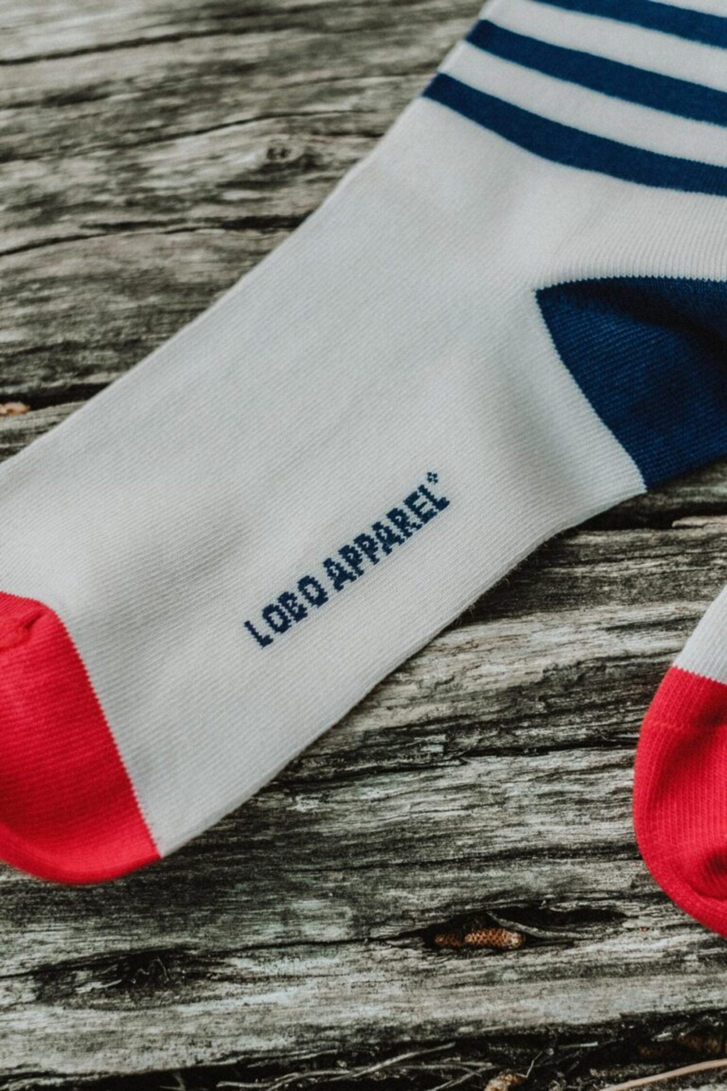 Detail of the Lobo blue striped sock featuring the Lobo Apparel branding on the sole and a red toe, displayed on rustic wood.