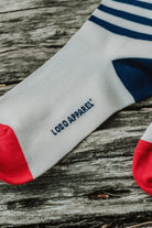 Detail of the Lobo blue striped sock featuring the Lobo Apparel branding on the sole and a red toe, displayed on rustic wood.