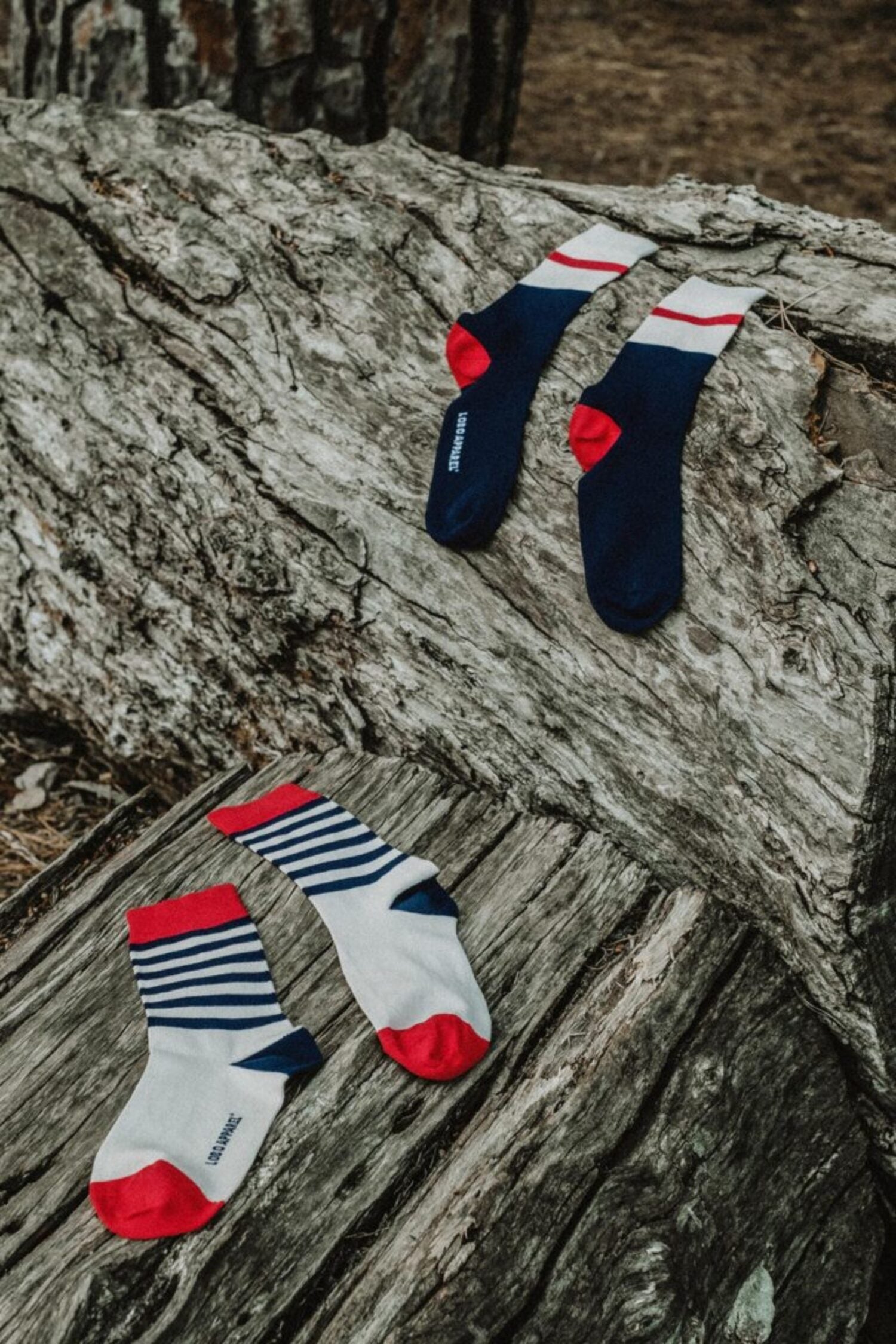 Set of two Lobo Apparel sock styles — nautical stripes and navy color block — made from premium natural fibers, displayed on a tree log.