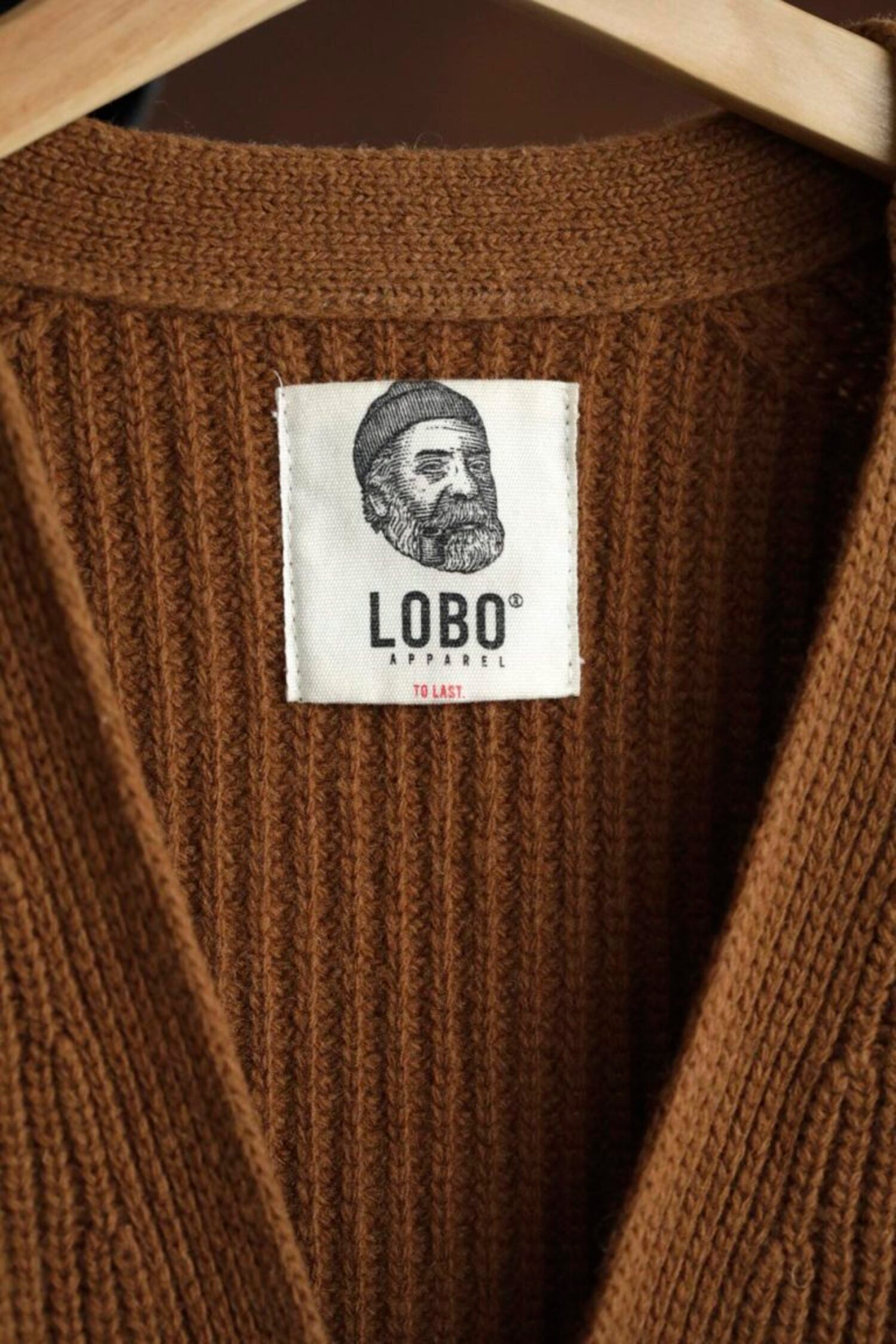 Close-up of Lobo Apparel "To Last" interior neck label on a high-quality brown knit cardigan.