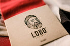 Close-up of Lobo socks' kraft paper packaging, showcasing the brand logo and the bearded man illustration over the Classic Red Socks fabric.