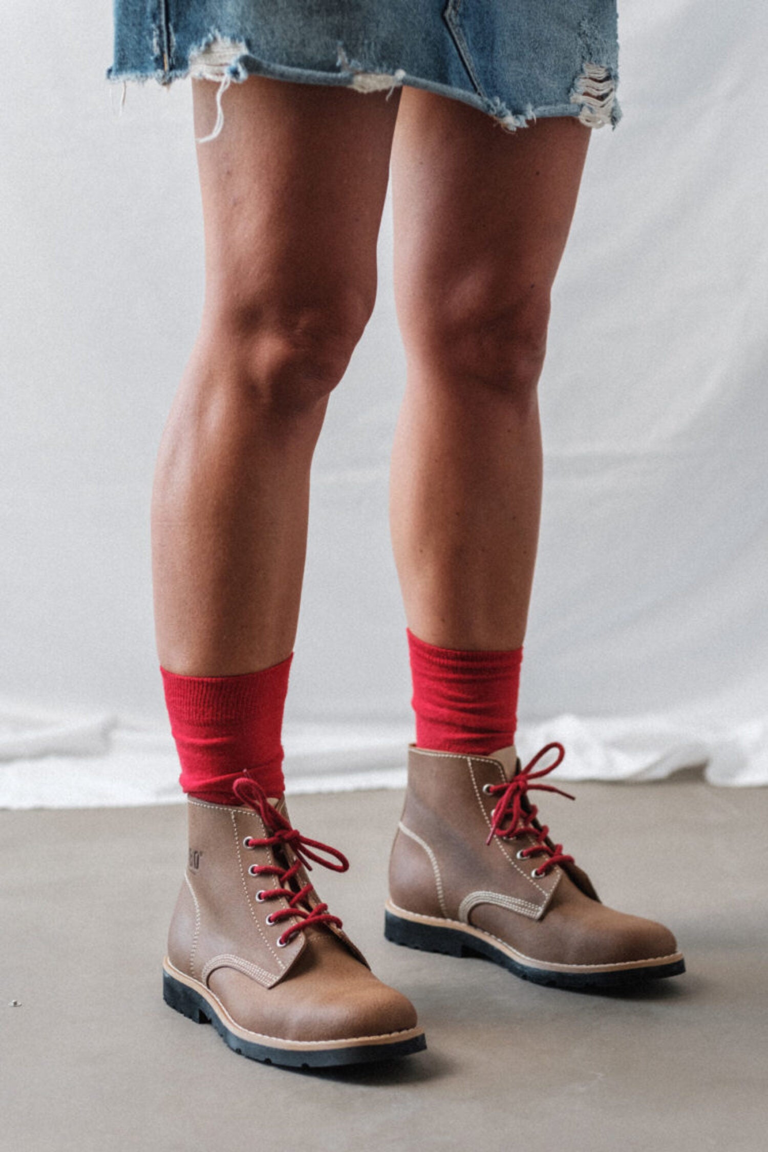 Woman wearing a denim skirt and brown leather boots with Lobo Classic Red Socks, highlighting the color contrast and the comfort of premium natural fibers.