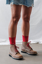 Woman wearing a denim skirt and brown leather boots with Lobo Classic Red Socks, highlighting the color contrast and the comfort of premium natural fibers.