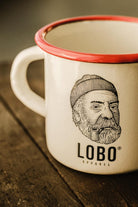 Close-up detail of the print on the LOBO enamel mug, highlighting the logo of the man with a beanie and pipe and the glossy finish.