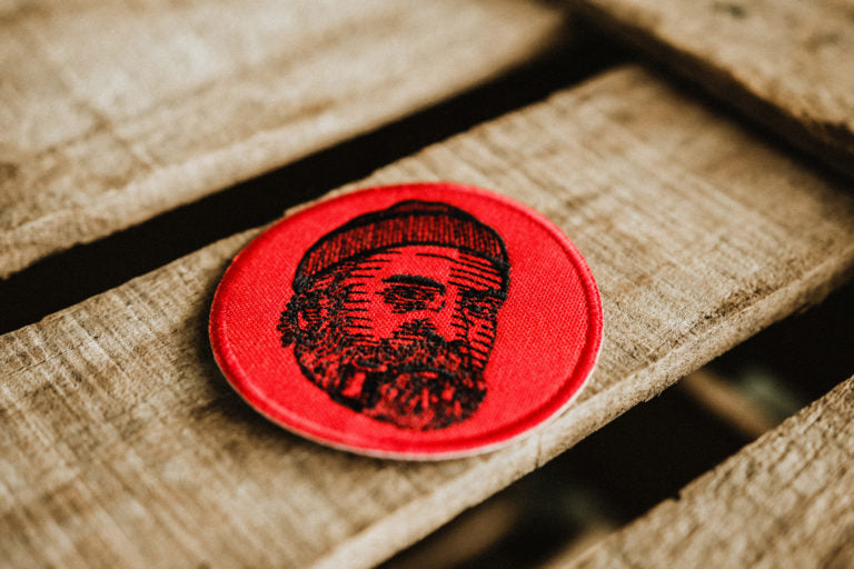 Lobo Face Round Red Patch, a 7 cm embroidered patch featuring a bearded man with a beanie, iron-on or sew-on clothing accessory.