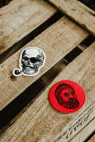 Lobo embroidered patch collection: red round patch with man's face and white pirate skull with pipe patch on a wooden background.