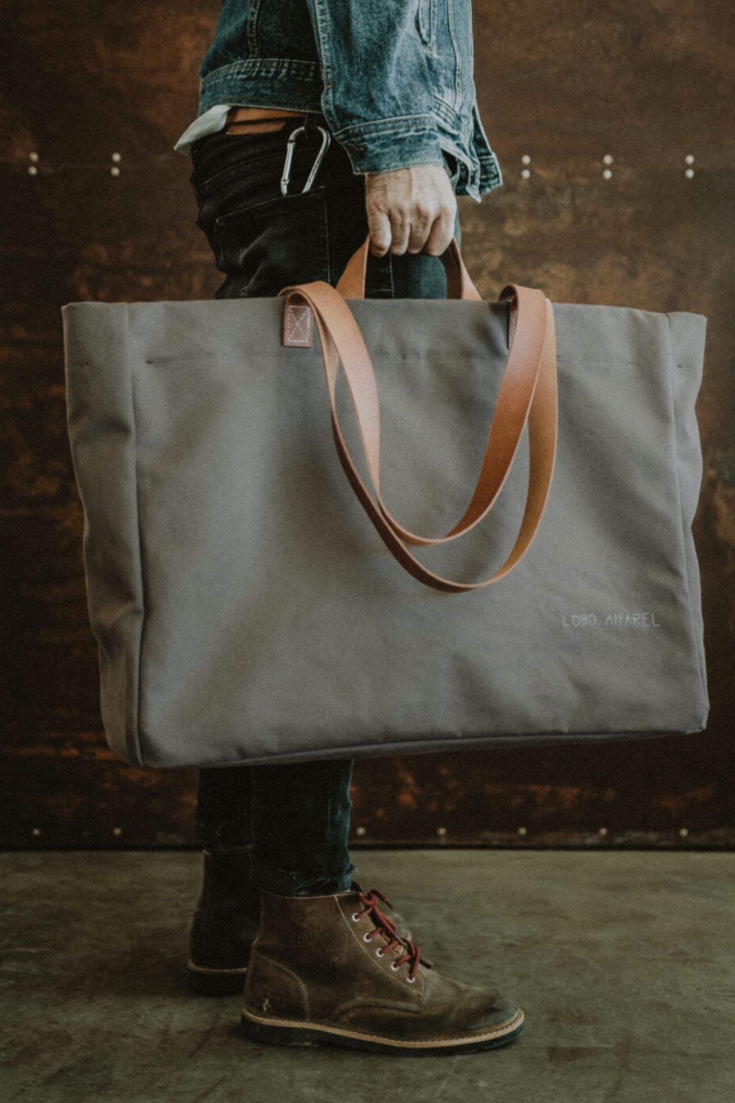 Man holding the Lobo Green Huge Bag in military green canvas with leather handles, showcasing its large size.