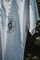Close-up detail of the grey t-shirt's chest pocket, showing the screen-printed Lobo emblem with a sailor illustration and the phrases "To Last" and "To Resist".