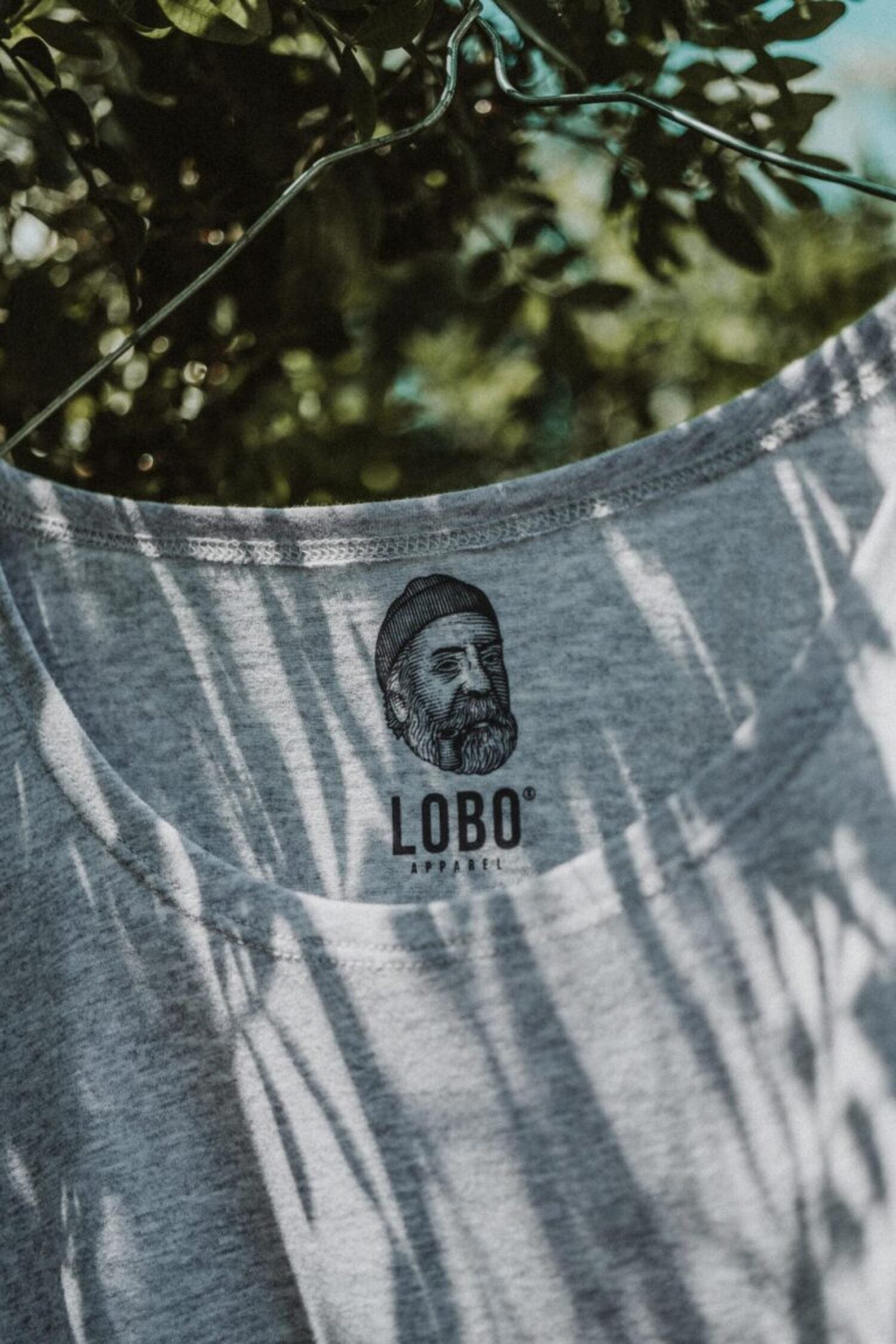 Detail of the Lobo Grey T-shirt's crew neck, showing the inner printed brand logo label under natural light and shadows.