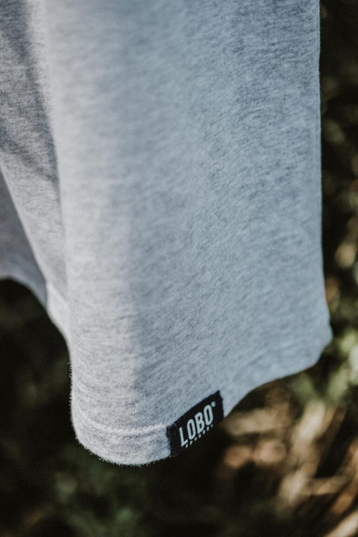 Close-up of the grey t-shirt's bottom hem, highlighting the small black woven label with the white Lobo logo.