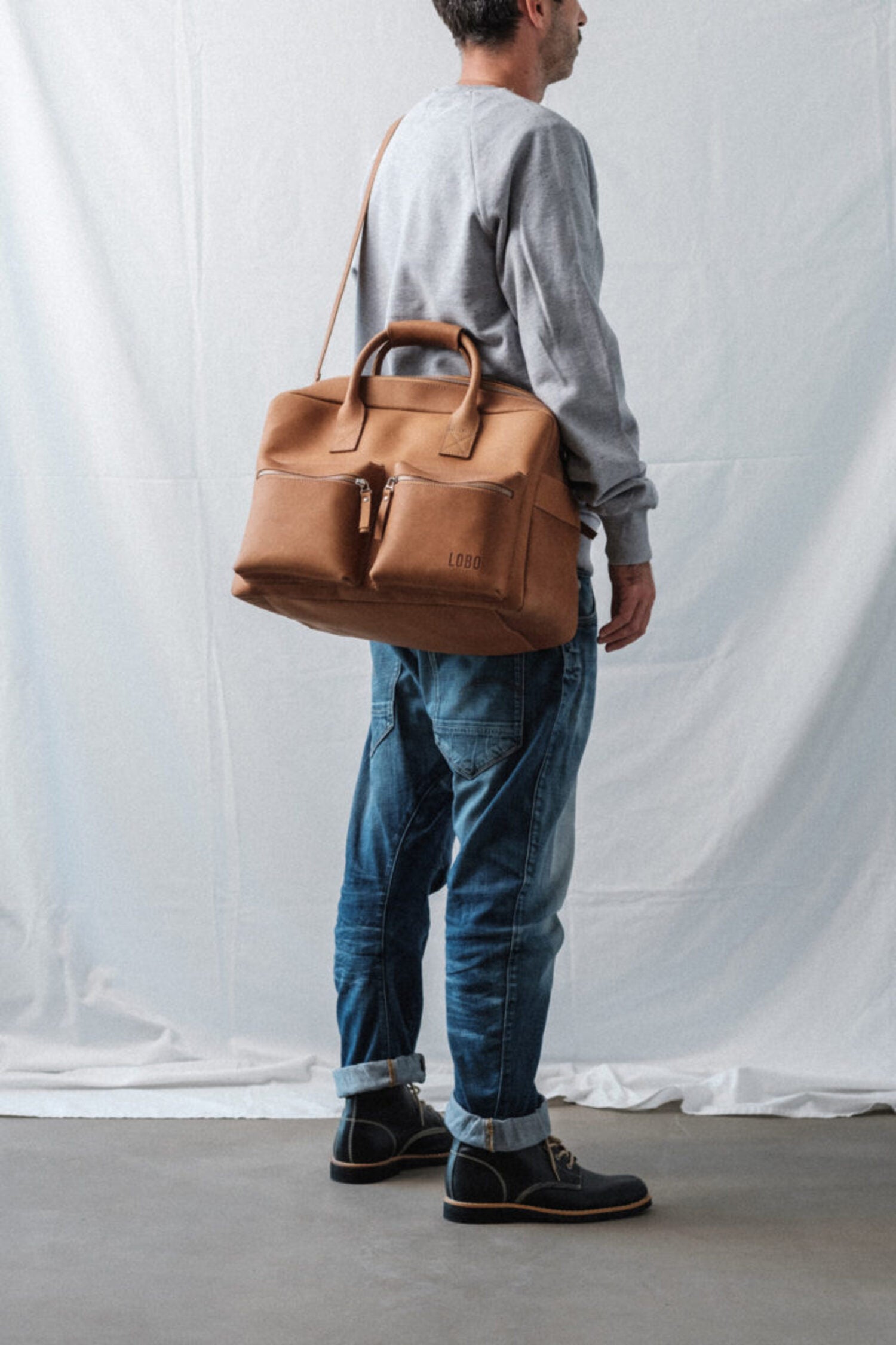 Man carrying the Lobo Leather Suitcase over the shoulder, showcasing the size and minimalist design of the premium leather travel bag.