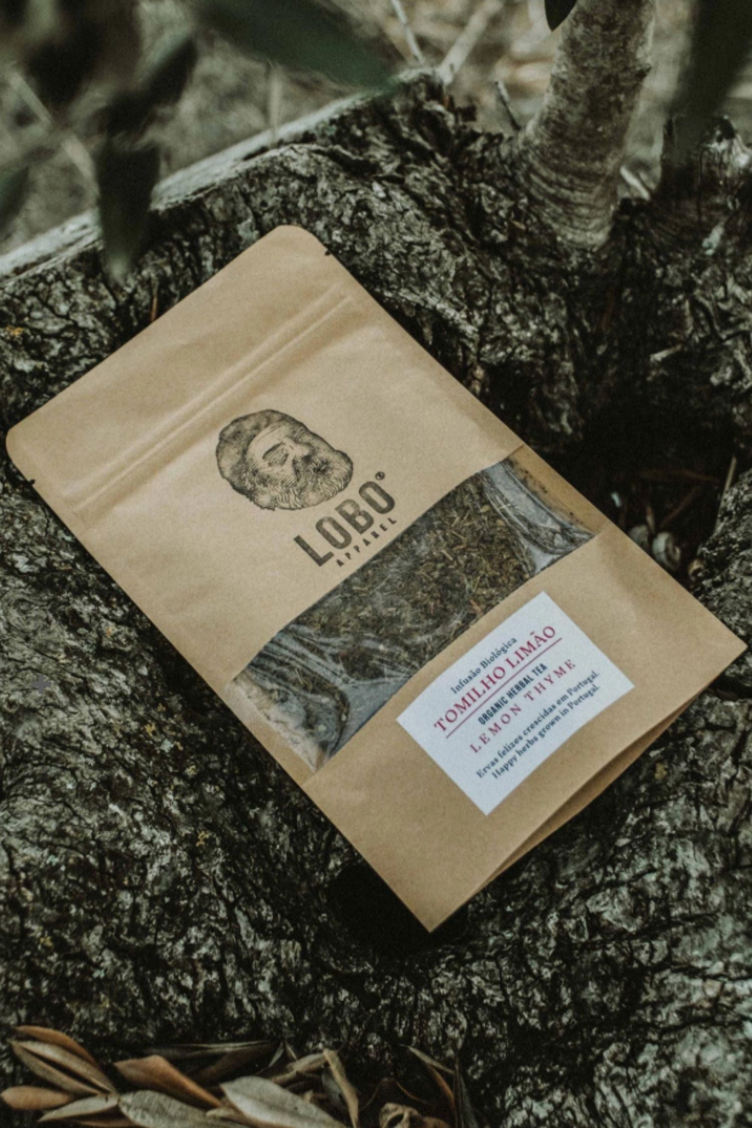 Kraft paper packaging of Lobo Lemon Thyme Organic Tea placed on a tree trunk in a natural setting.