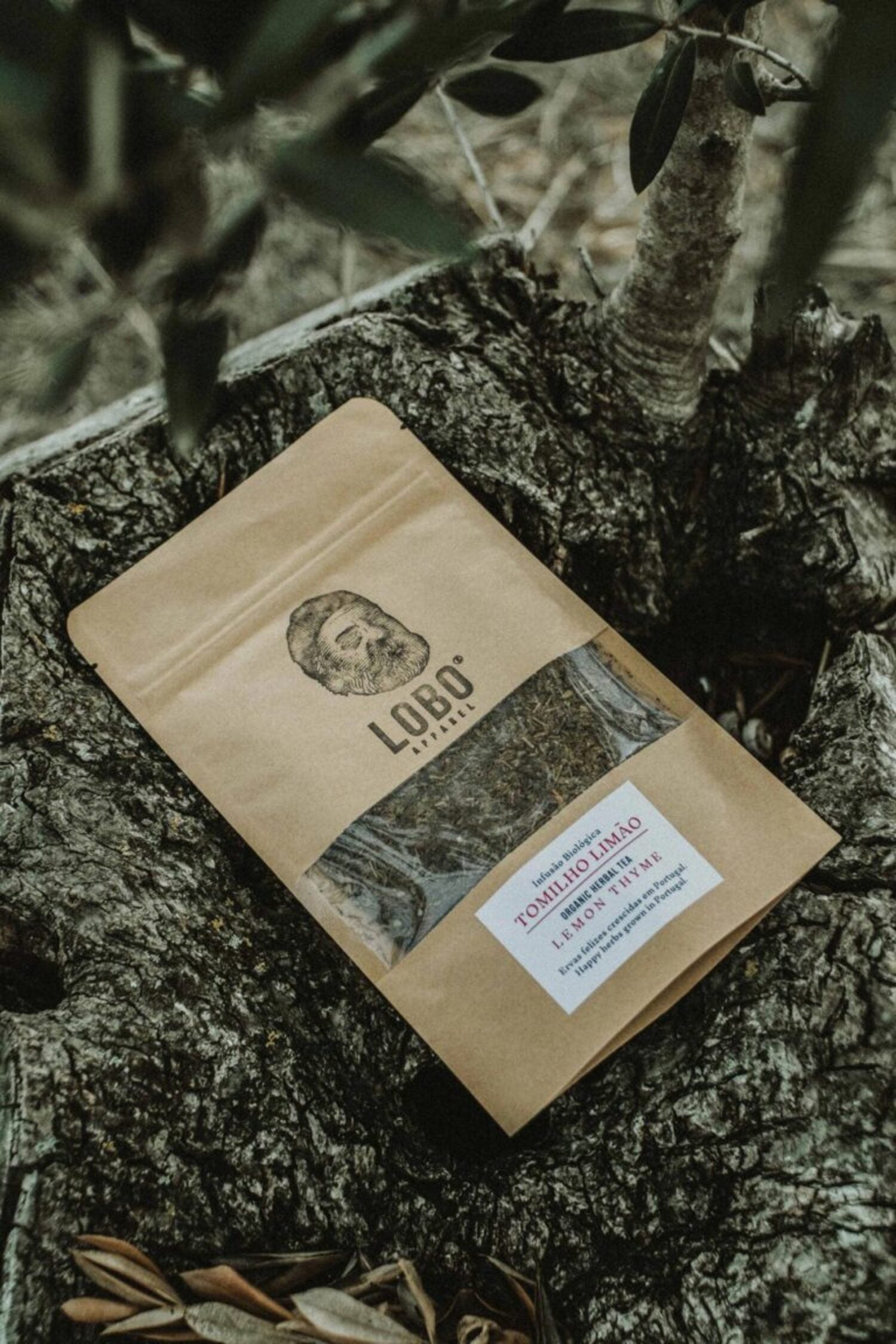 Kraft paper packaging of Lobo Lemon Thyme organic herbal tea placed on a rustic tree trunk.