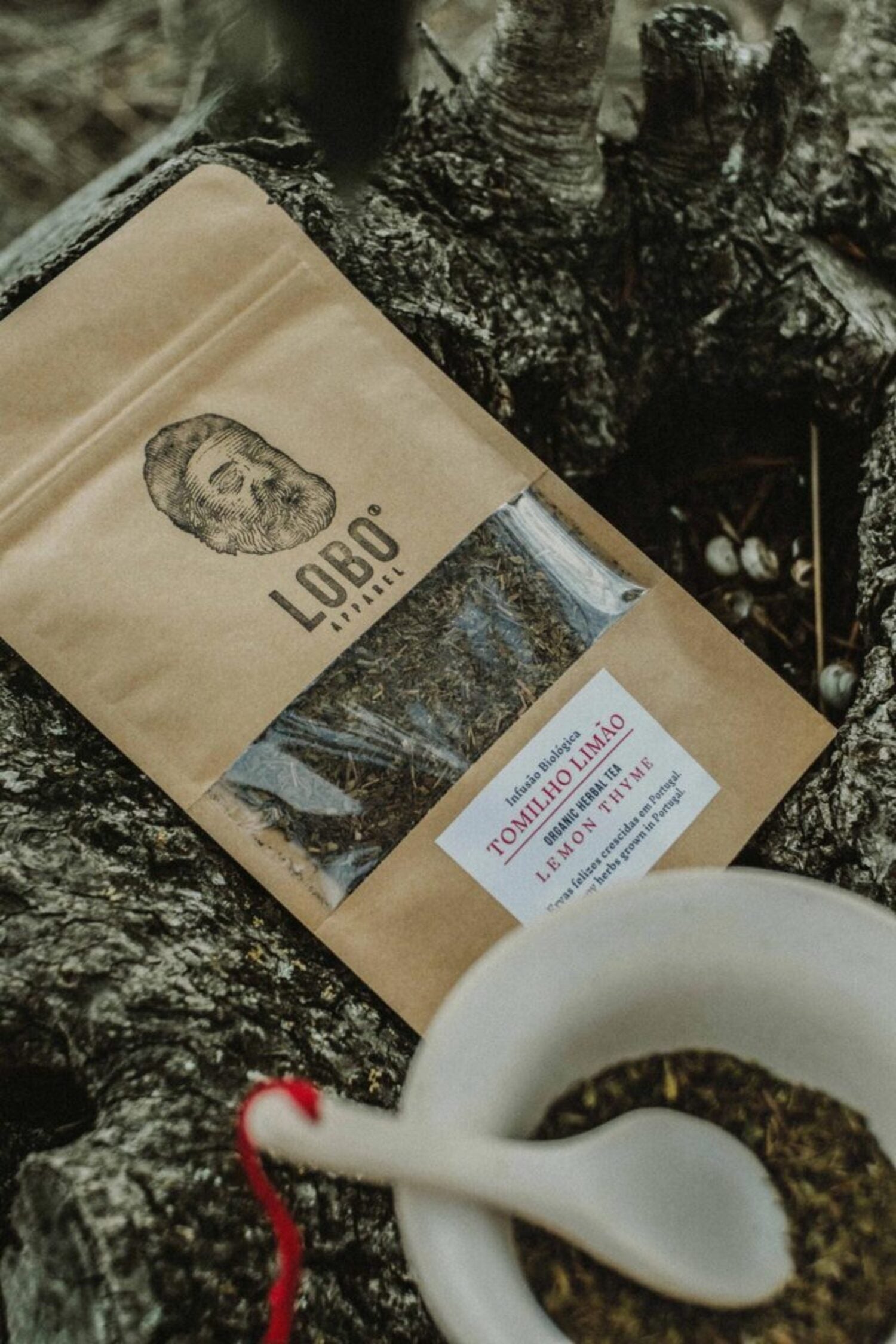 Preparing Lobo Lemon Thyme organic herbal tea with a ceramic bowl and spoon, set on a rustic tree trunk in a natural environment.