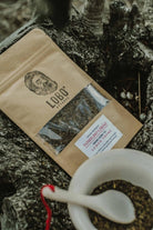 Preparing Lobo Lemon Thyme organic herbal tea with a ceramic bowl and spoon, set on a rustic tree trunk in a natural environment.