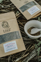 Two packages of Lobo Organic Lemon Thyme herbal tea next to a bowl of dried herbs, arranged on a natural ground of leaves and twigs.