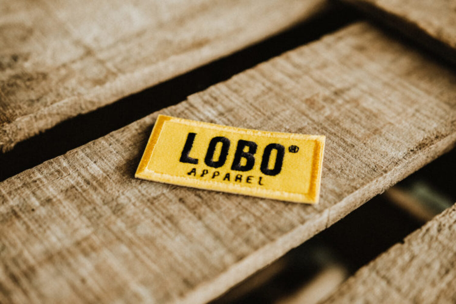 Yellow Lobo Apparel embroidered logo patch 6x3 on wood, official iron-on or sew-on clothing accessory.