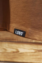 Close-up of the small black hem tag with the white "LOBO" logo at the bottom of the "Natureza" t-shirt.