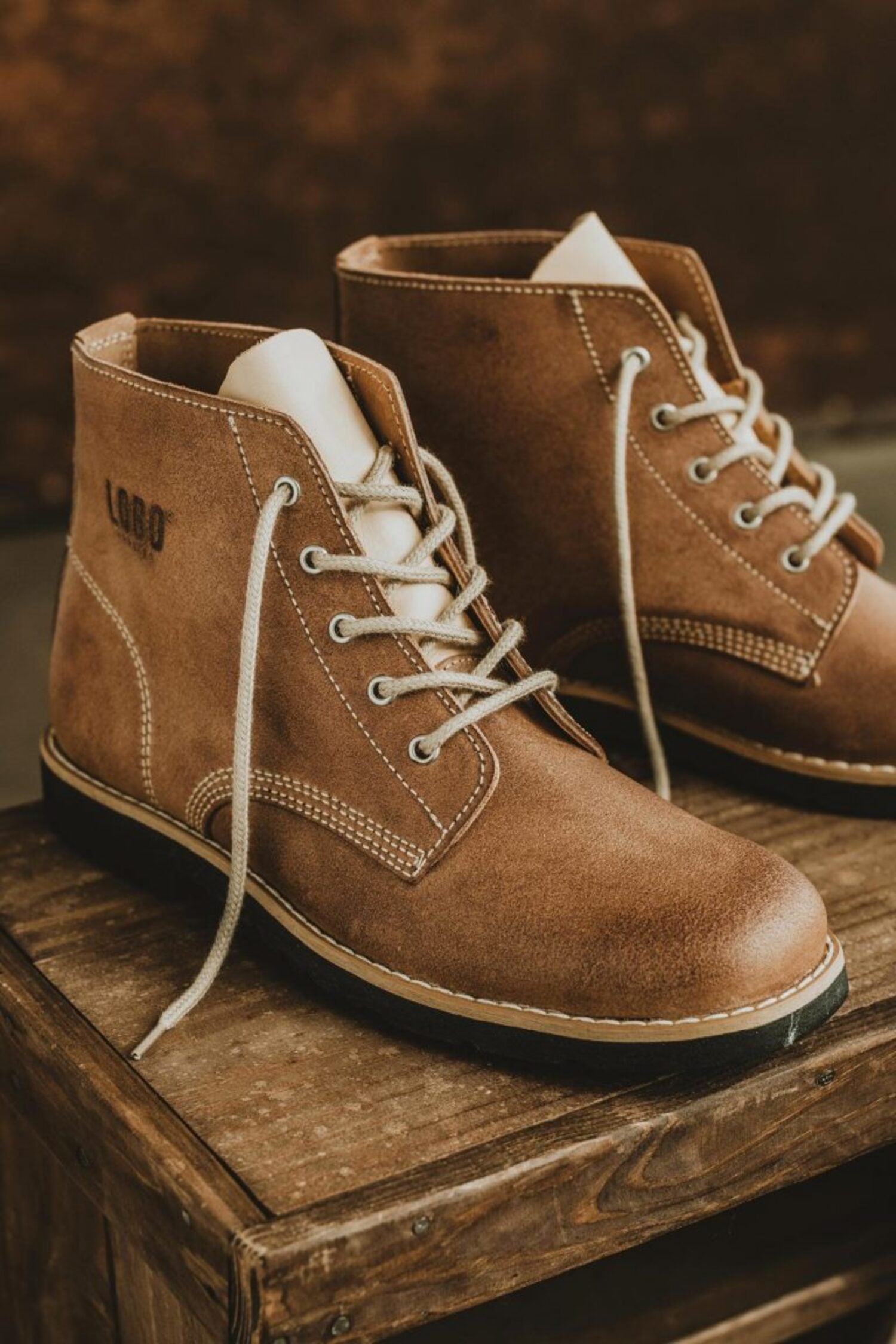 Detail shot of Lobo Raw brown leather boots featuring cream laces on a rustic wooden background.