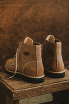 Rear view of Lobo Raw brown leather boots on a rustic wooden stool, highlighting the branded logo stamp.