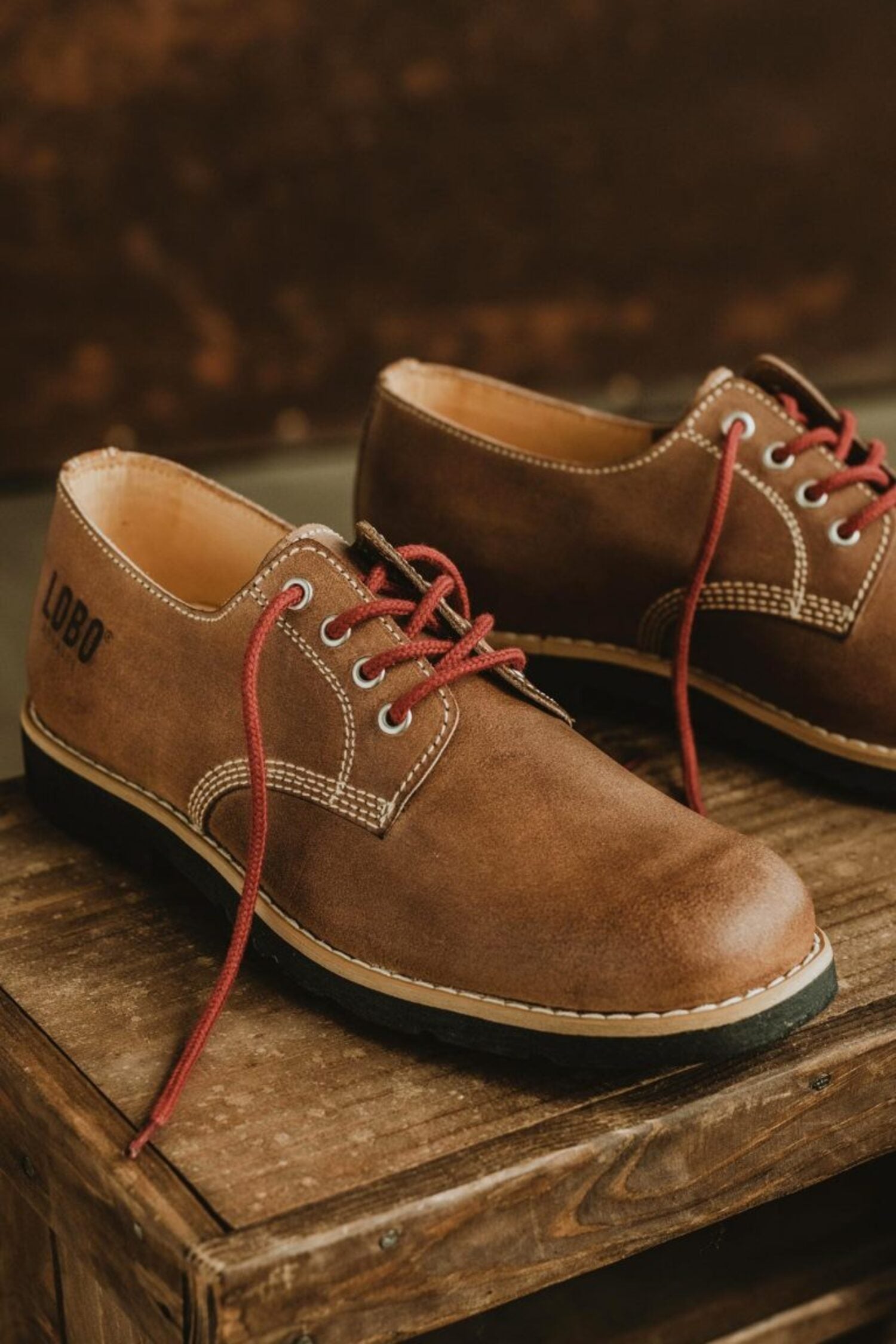Lobo Raw leather shoes in brown with red laces, Goodyear Welt construction on a rustic wooden surface.