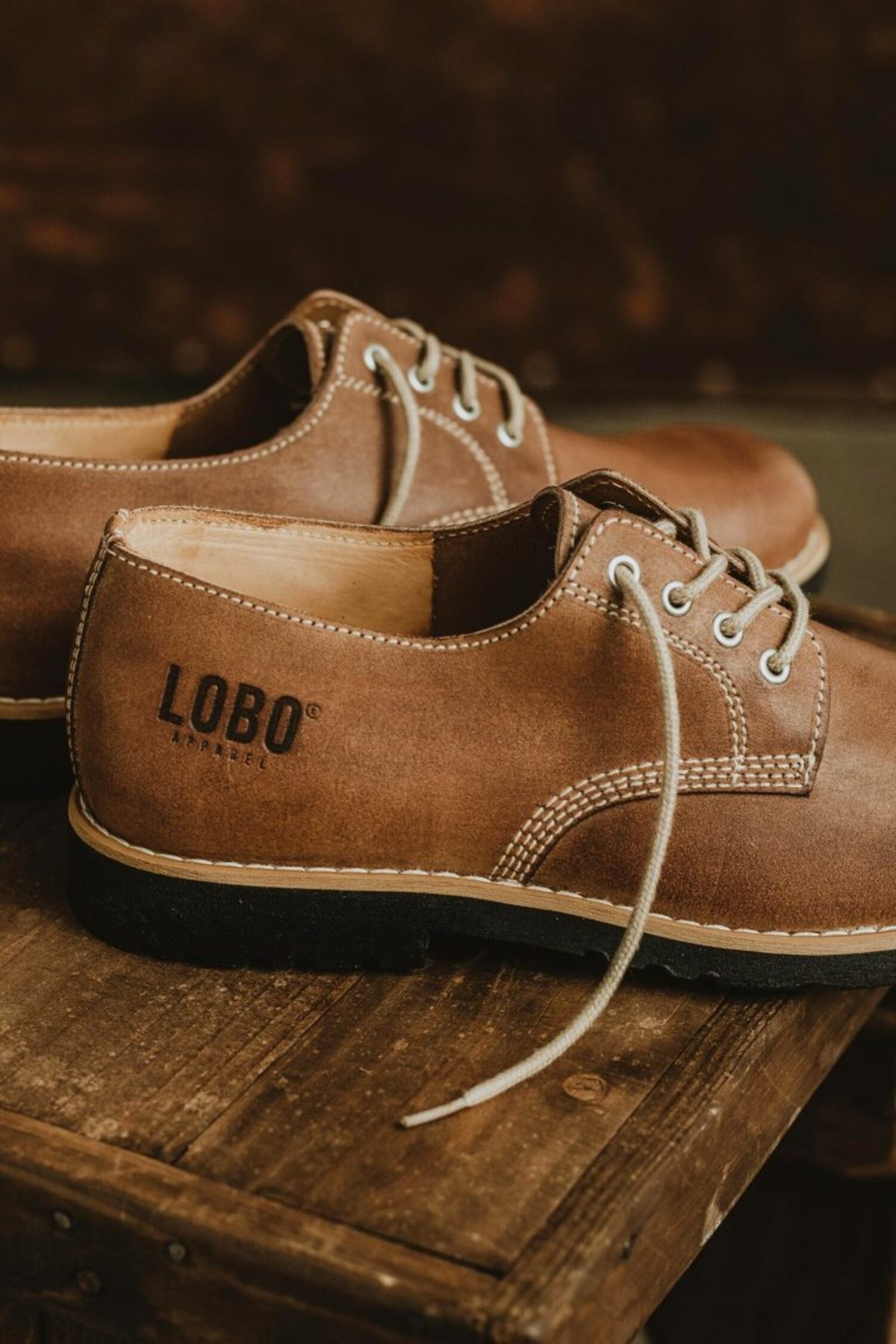 Side view of brown leather shoes with Lobo Apparel logo embossed on the heel and black rubber sole.