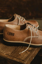 Side view of brown leather shoes with Lobo Apparel logo embossed on the heel and black rubber sole.