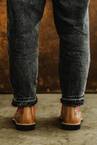Rear view of a person wearing Lobo tan leather boots with dark wash jeans, showing red side panels.