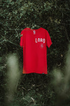 Lobo red premium cotton t-shirt hanging on a tree branch, showing the "LOBO" screen print and front pocket detail.