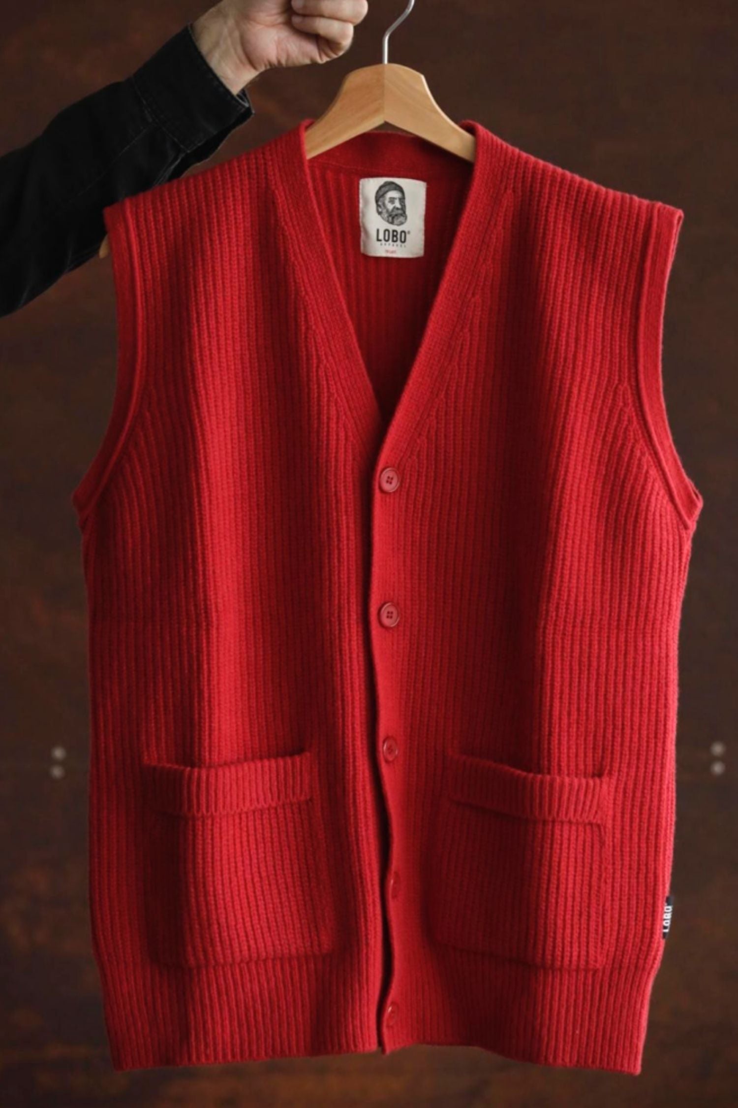 Red wool knit Lobo Red Vest hanging on a wooden hanger, showing the knit texture, front buttons, and the Lobo brand label.