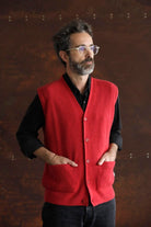 Bearded man with glasses wearing the Lobo Red Vest, a unisex red wool vest, over a black shirt against a rustic background.