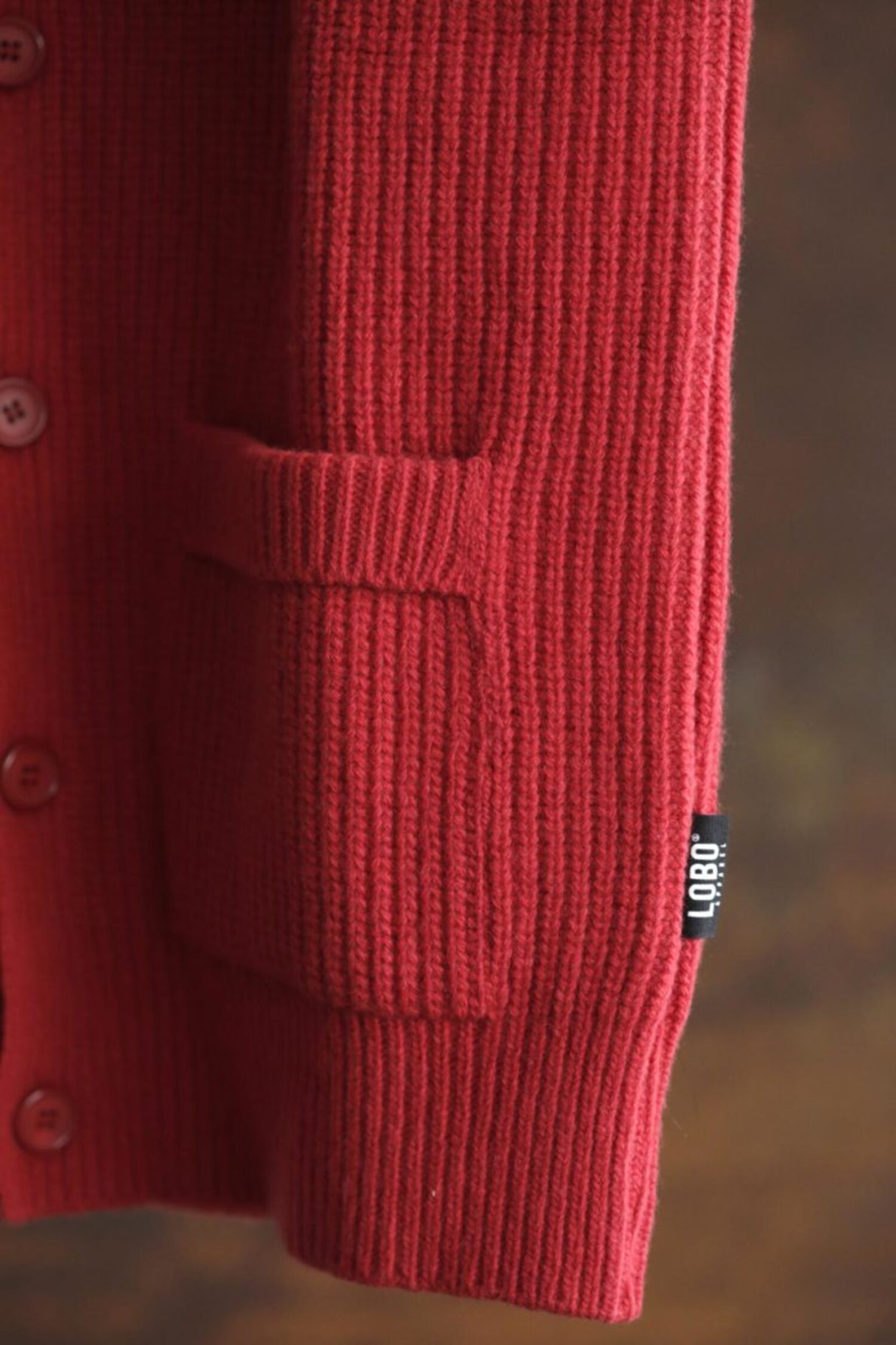 Close-up of the red ribbed wool knit on the Lobo Red Vest, showing the front pocket, buttons, and the small black Lobo brand tag.