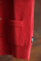Close-up of the red ribbed wool knit on the Lobo Red Vest, showing the front pocket, buttons, and the small black Lobo brand tag.