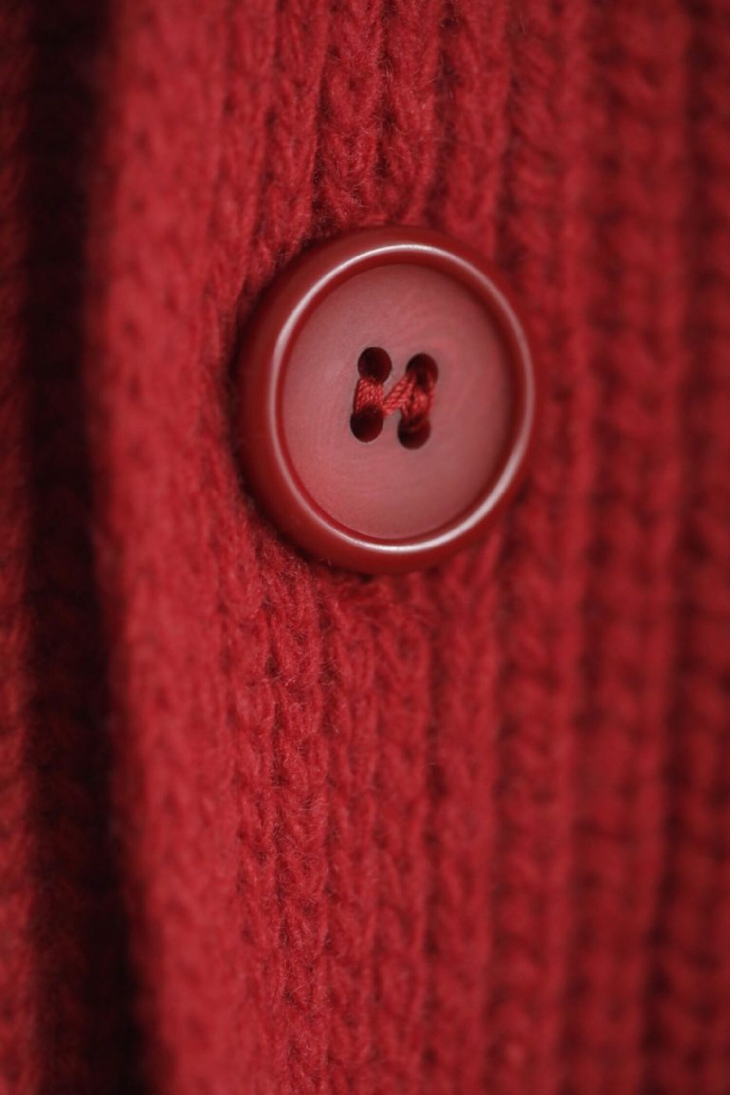 Close-up of a red button on the Lobo Red Vest wool vest, highlighting the ribbed knit detail and handcrafted finish.