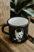 Lobo Skull black enamel mug featuring a skull smoking a pipe illustration, resting on rustic wood.